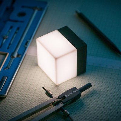 Würfelförmige Mini-Leuchte mit weißem Lichtwürfel und schwarzem Rahmen auf Schreibtisch