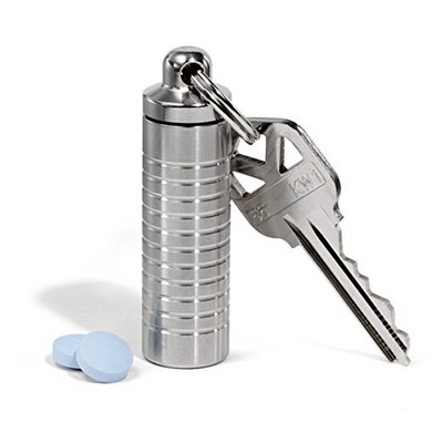 Schmale silberne Pillendose aus Edelstahl am Schlüsselbund, daneben zwei blaue Tabletten